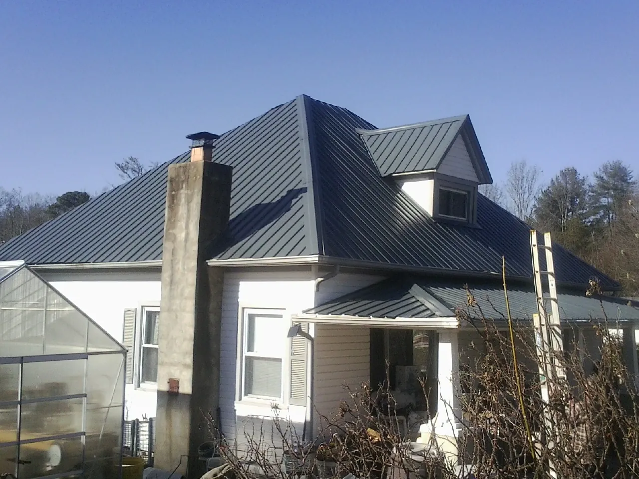 Dark blue standing seam metal roof on a white farmhouse with dormer — Slate & Tile Roof Repair by Roofing Brothers in Renville