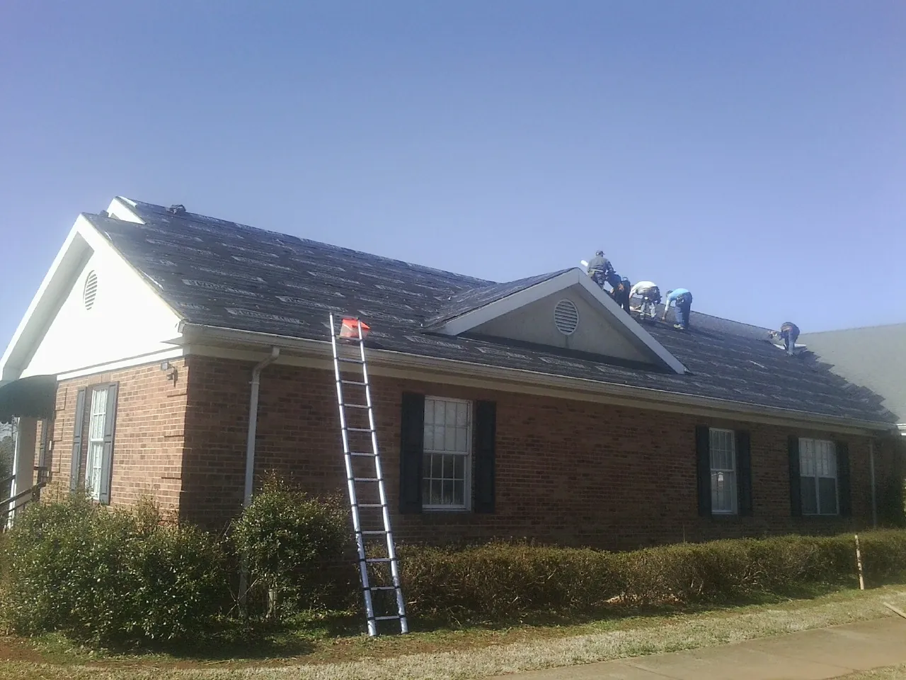 Crew tearing shingles off a brick ranch roof with a ladder set — Emergency Roof Repair work by our crew in Renville