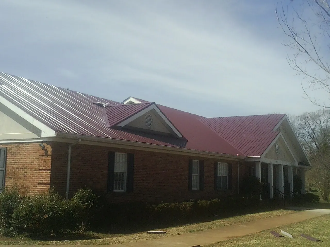 Red metal roof with gabled entries on a long brick building, from a Hail Damage Roof Repair job in Renville