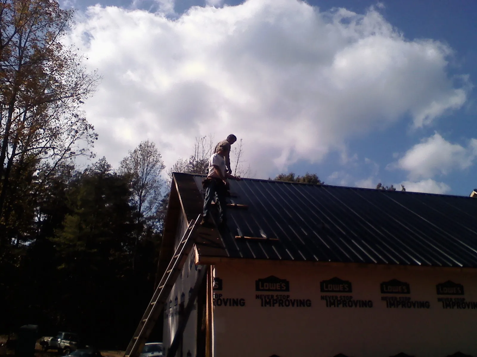 Roofer fastening dark metal panels high against a cloudy sky, from a Roof Inspection job in Renville