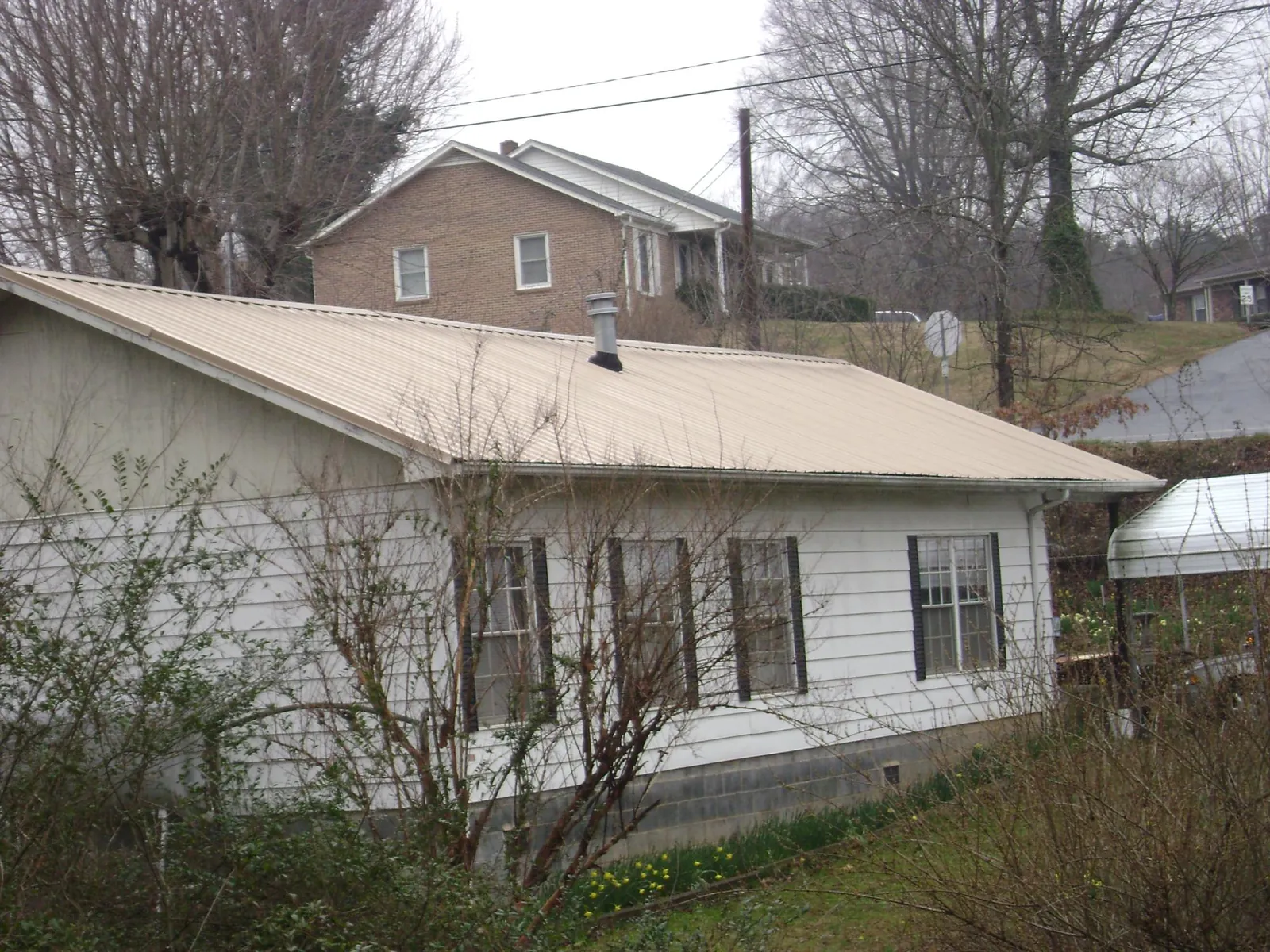Tan metal roof on a white sided house set into a hillside — Commercial Roofing by Roofing Brothers in Renville