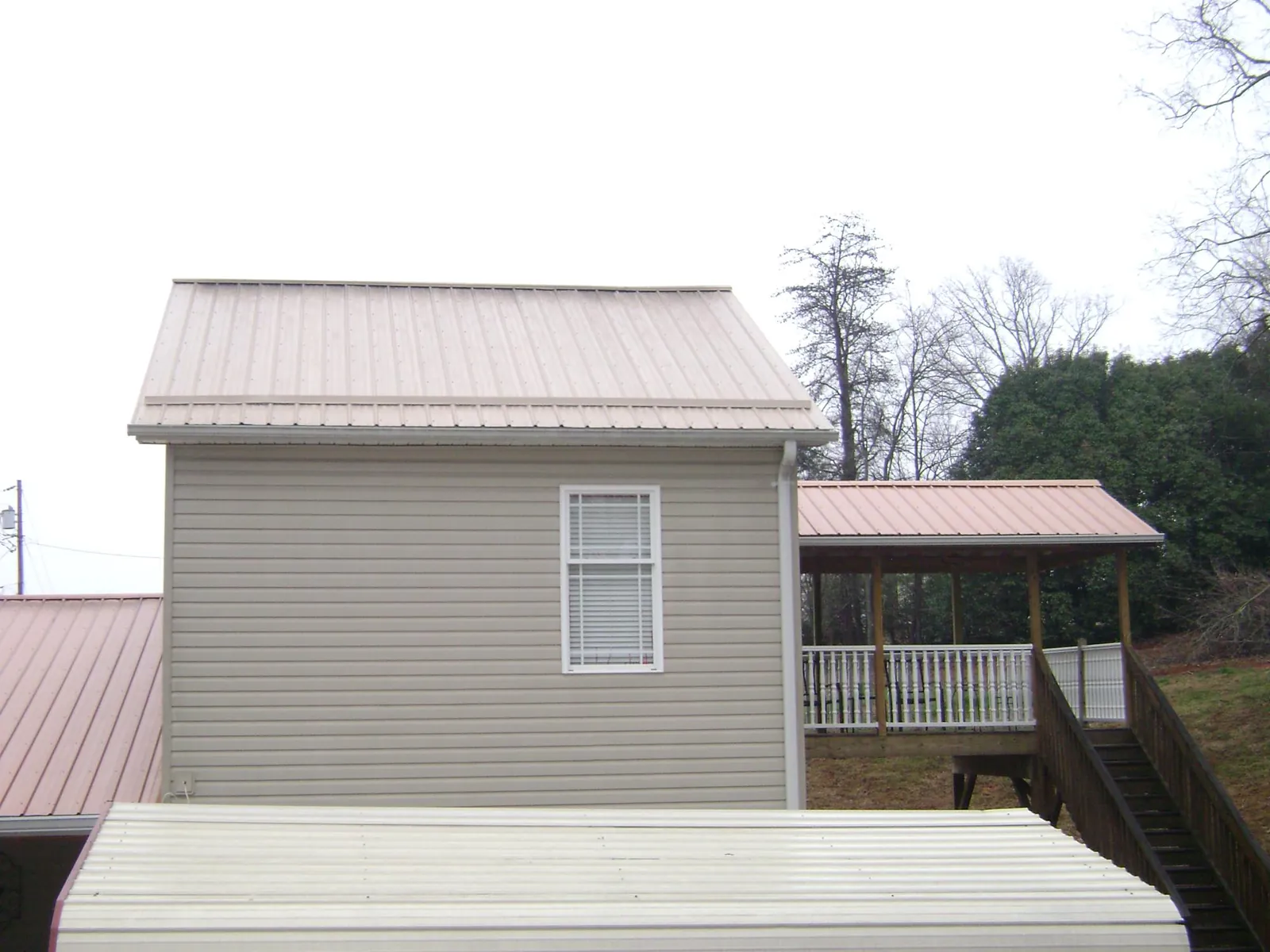 Tan metal roofs on a two story addition and attached porch, from a Roof Replacement job in Renville